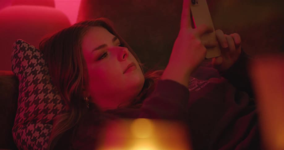 A woman reclining on a couch smiles while looking at her phone