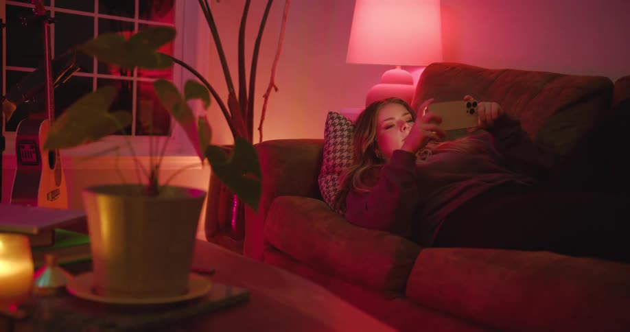 A woman laying on her back on a couch holds up her smart phone
