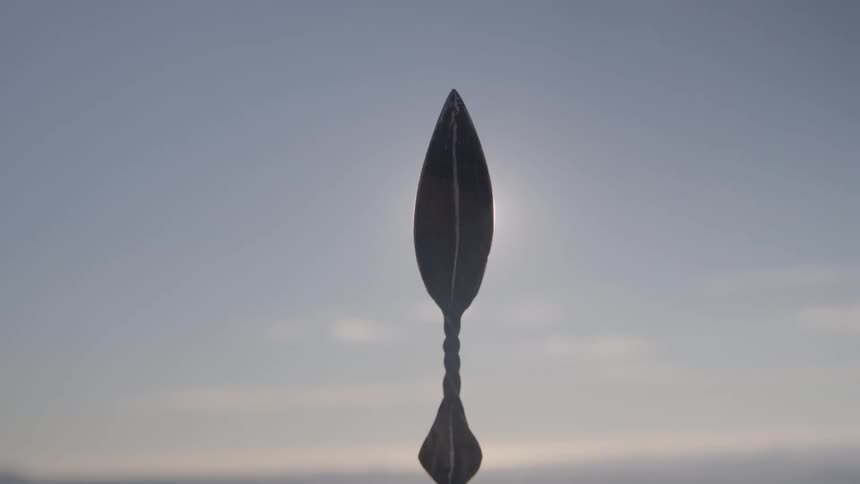 The tip of a metal spear with the sun shining brightly behind it