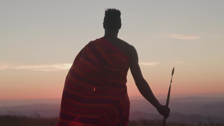 A man stands atop a hill holding a spear