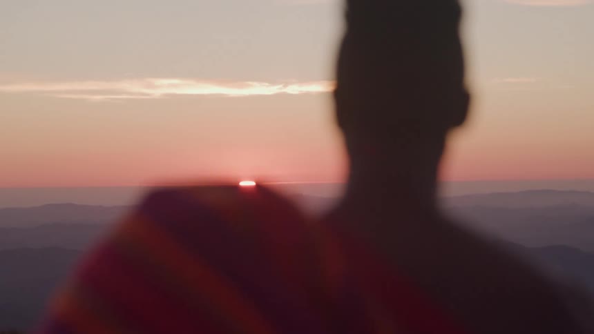 A person standing looking at the horizon where the sun is rising and turning the whole sky orange