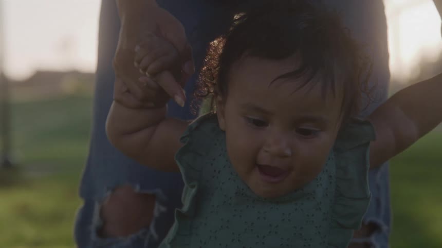 A young toddler practices walking with the help of an adult