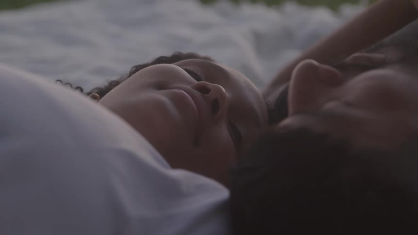 A couple lay together on a blanket on the grass