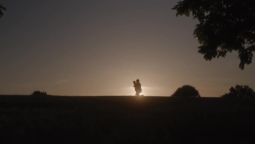 A boy runs into his fathers arms outdoors at sunset