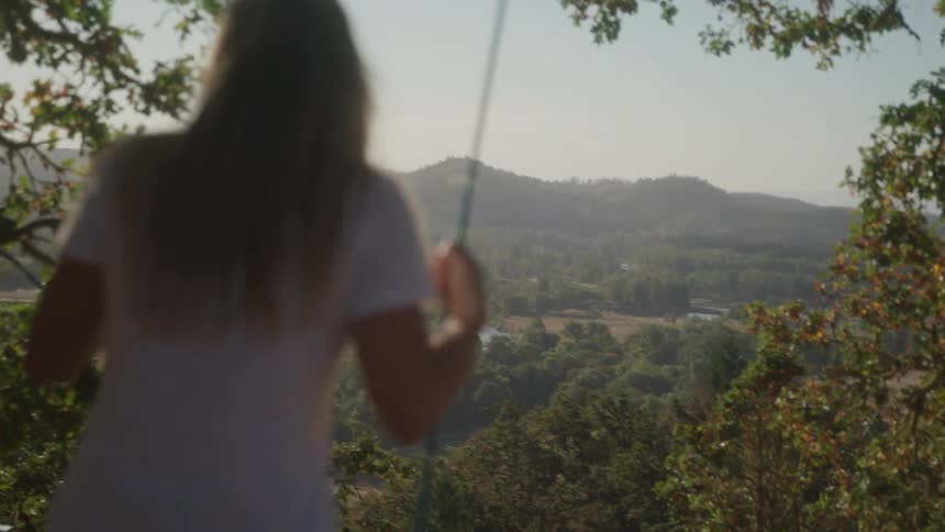 A female swings on a lone swing overlooking a scenic valley