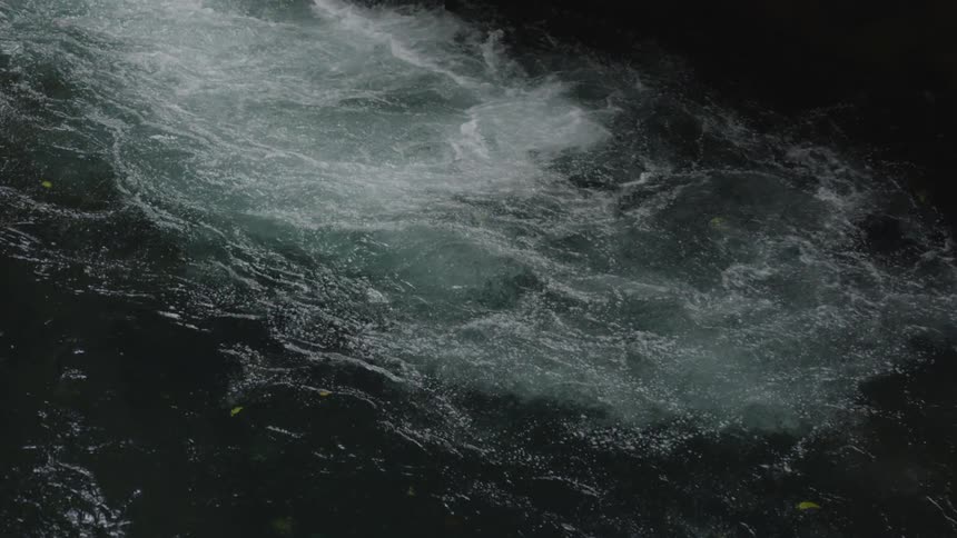 The video shows an overhead shot of a body of water likely a river or stream the water is churning and white with foam in some areas while other parts are dark and still
