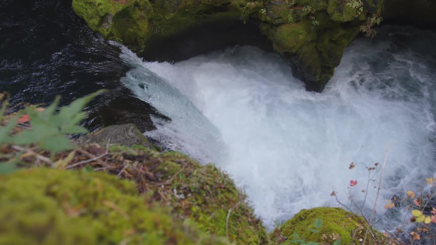 A view from a rocky moss covered cliff looks down on a churning white water river rushing past dark rock