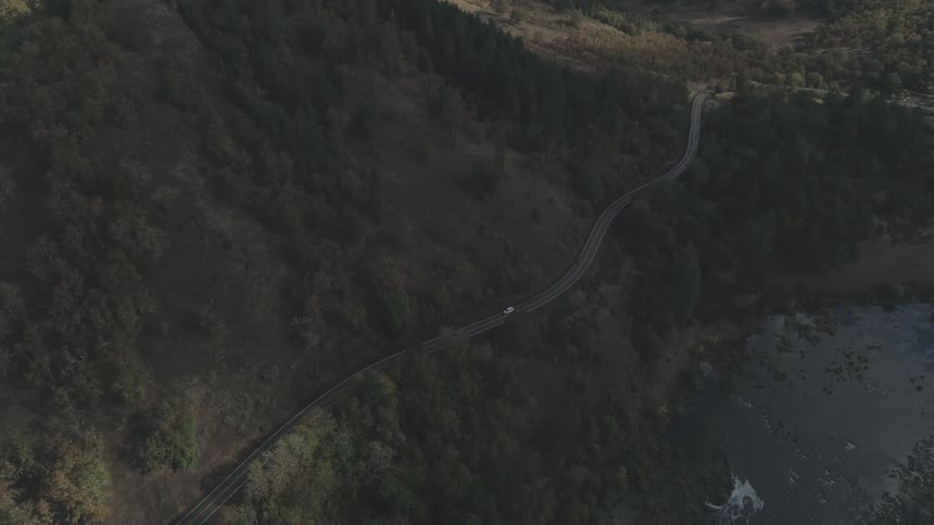 An aerial view of a road with a car passing between hills full of trees