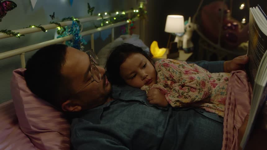Daughter lies against her father while the man reads her a bedtime story