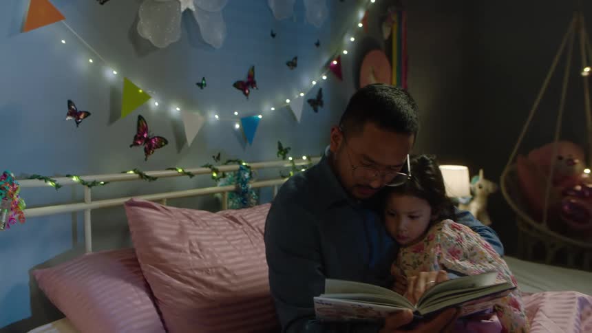 Father reads a bedtime story to his daughter in a cozy bedroom