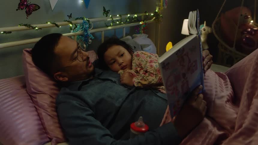Father reads a bedtime story to his daughter in a decorated bedroom at night