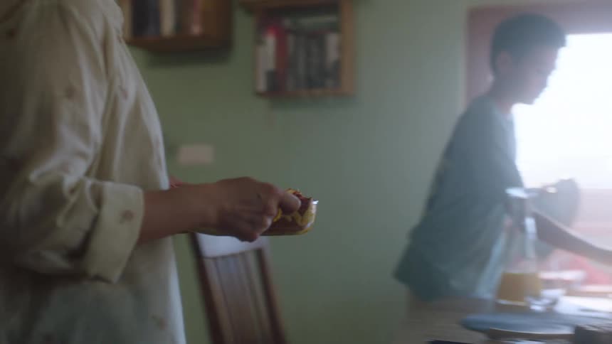 The video shows a family in a kitchen preparing food together a man helps a young child mix a bowl of flour while a woman walks through the kitchen carrying a dish in the background a boy walks past