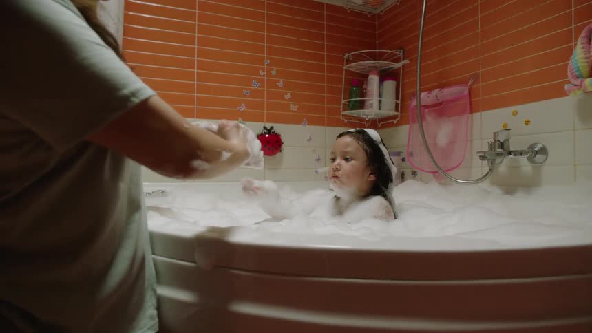 A mother giving her daughter a bath in a bathtub in the bathroom at midday