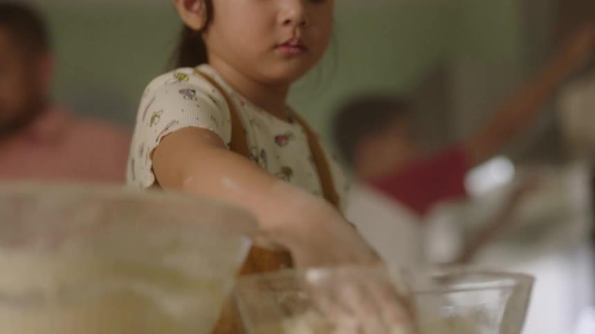 A young girl kneads dough in a glass bowl at home kitchen
