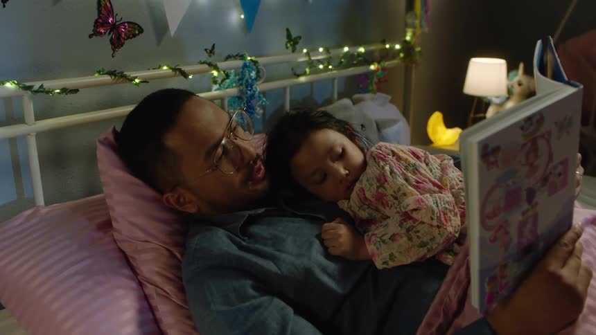 Father reading a book to his daughter lying on his lap in a decorated room