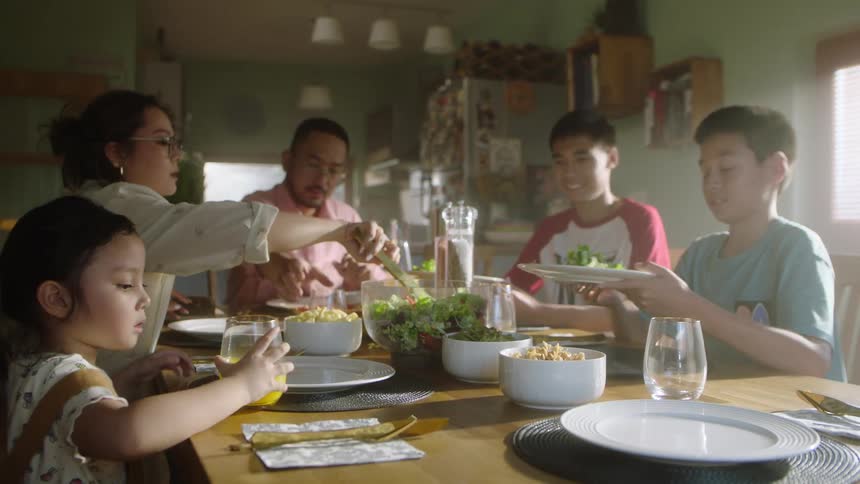 A family eats together as the mother serves food at the table