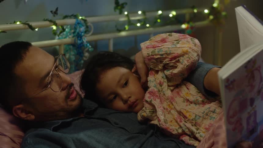 Father reads a bedtime story to his daughter cuddled beside him at night