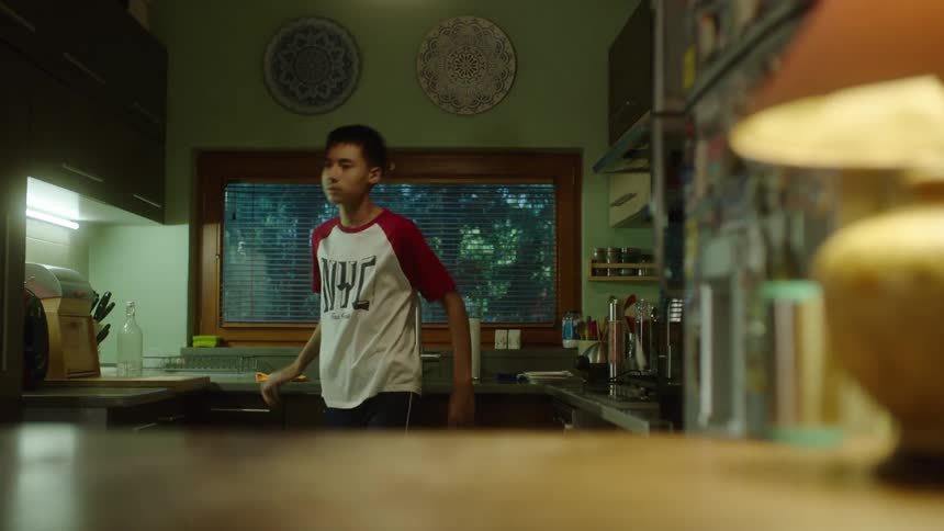 The video shows a person in a kitchen with a modern simple design including a wooden island and countertops in the foreground there is a lit lamp with a beige shade the person is holding up and looking at a dish towel before wiping the counters