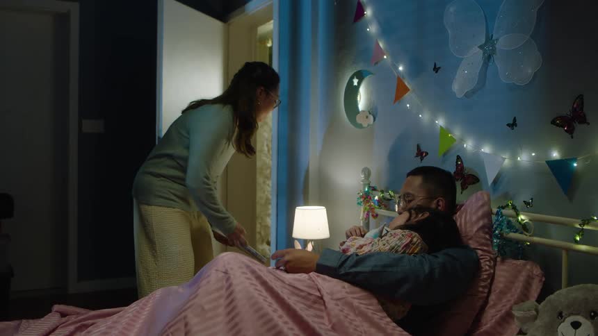 Mother enters the bedroom and takes the book as father and daughter sleep