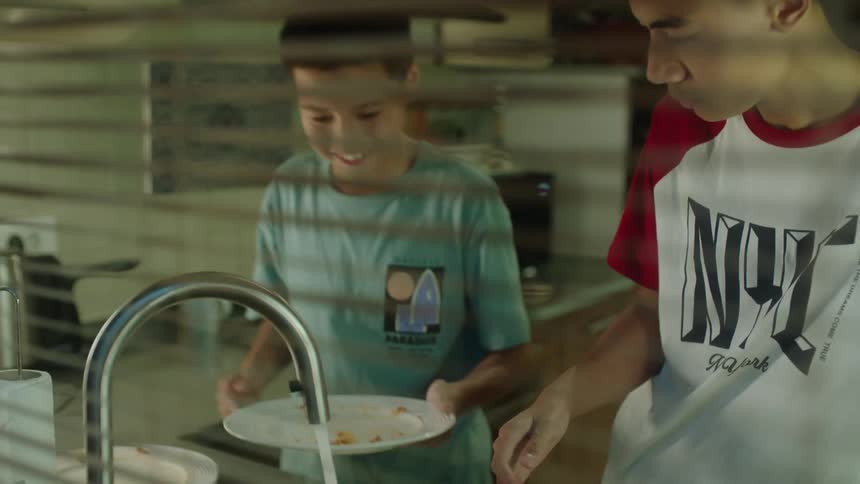 Two brothers clean dishes together in the home kitchen