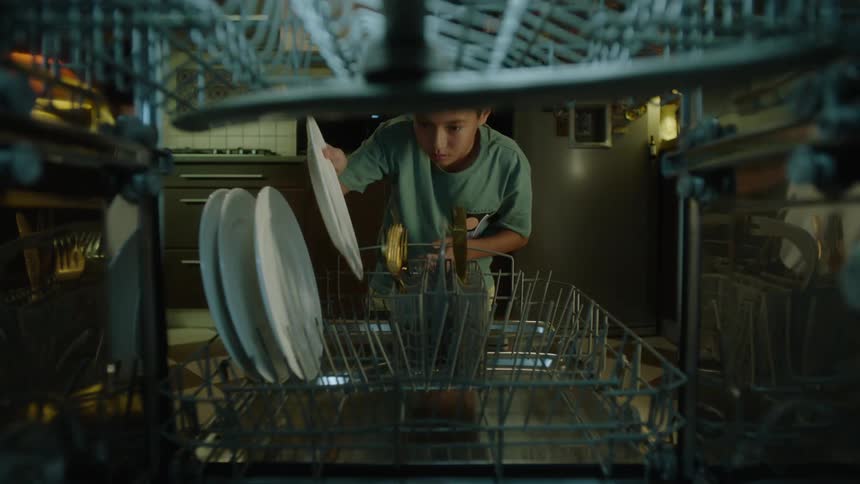 A boy loads dishes into a dishwasher in the kitchen