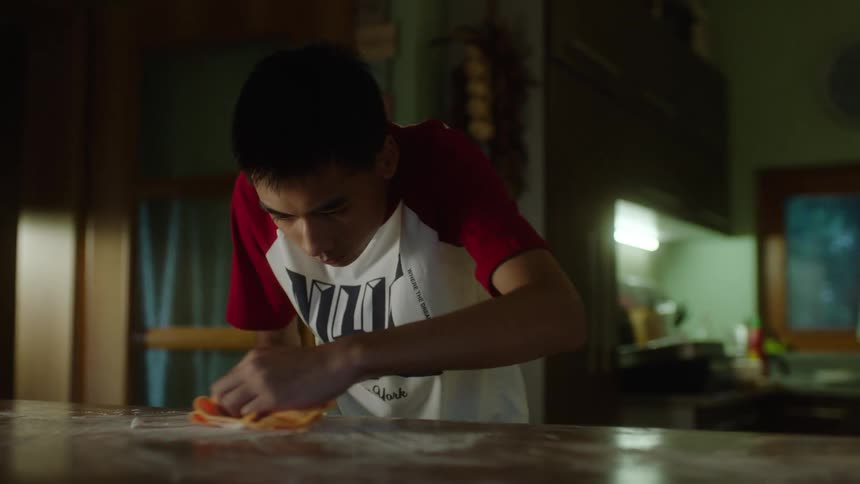 A boy wipes the kitchen counter while cleaning at home
