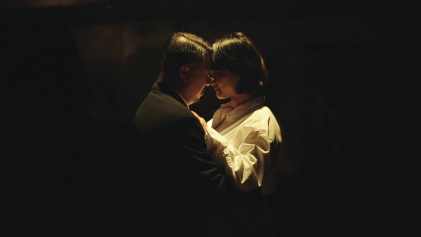 A man and a woman are standing face to face in a dark room they are standing very close to each other and the light is focused on the woman and her face