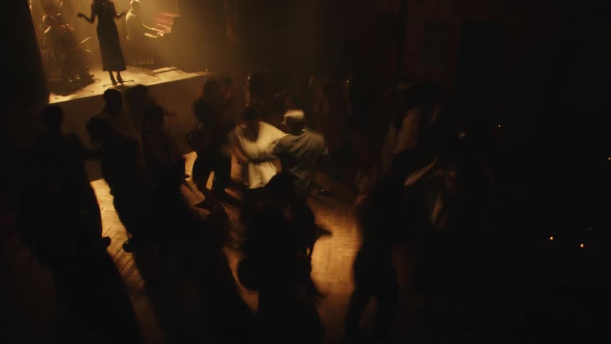 Crowd dances in a dimly lit hall as a live band plays on stage