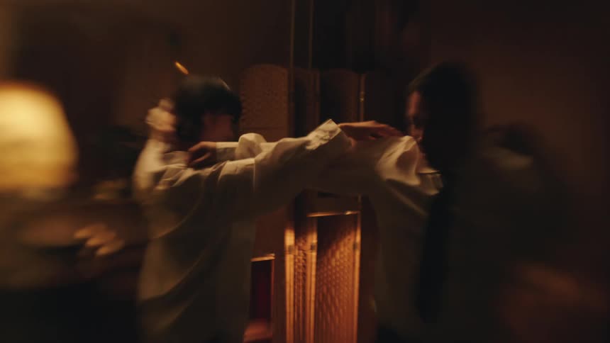 In a warm and dimly lit room a couple is seen dancing playfully and romantically