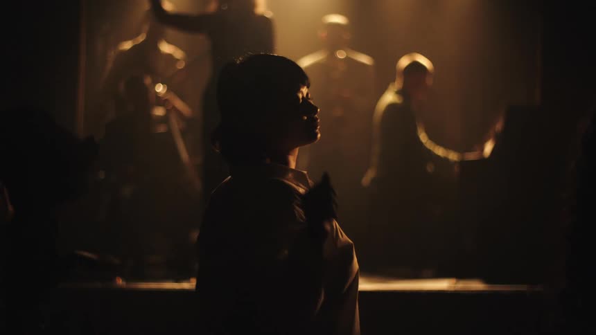 Silhouetted person dances with arm raised before live band