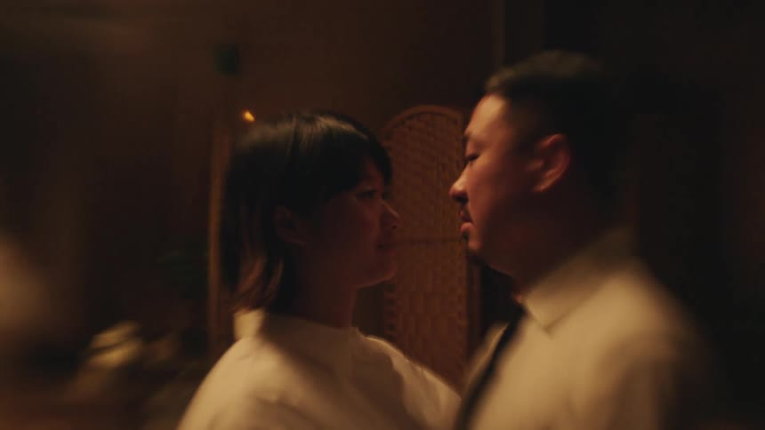 A man and woman are seen in a close embrace looking into each others eyes in a dimly lit intimate setting