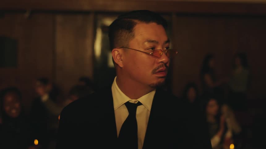 A man walks through a dimly lit bar filled with seated patrons and background conversation