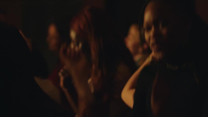 A group of people are seen enjoying themselves in a dimly lit crowded space swaying and dancing to music