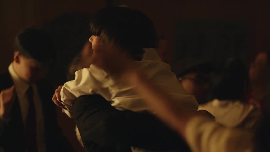 The video shows a group of people appearing to be at a celebration or party in a dimly lit room a man and a woman embrace in a hug with the mans hands on her waist and her arms wrapped around his neck