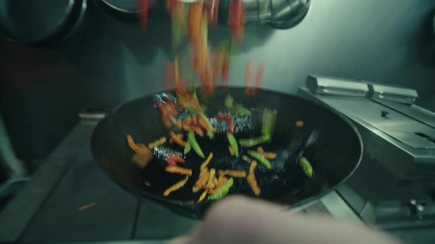 A chef stirring ingredients by hand in a frying pan in the kitchen