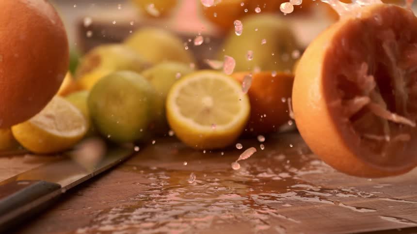 A whole grapefruit is dropped onto a cutting board where it splashes water and citrus juice the fruit breaks open revealing the juicy inside