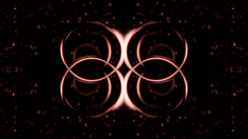An animated shot of an abstract symmetrical pattern of pulsing and morphing orangered light resembling a kaleidoscope effect on a black background with glowing particles
