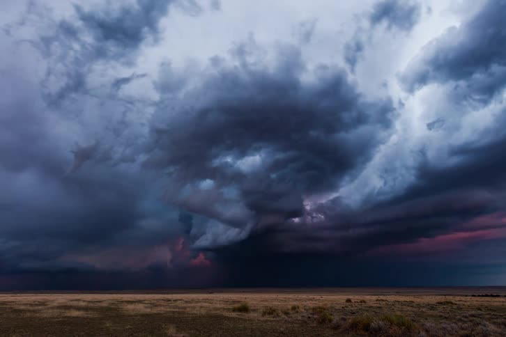 A dark ominous funnel cloud forms in the sky over a grassy field the storm clouds are churning and a flash of lightning is visible in the distance