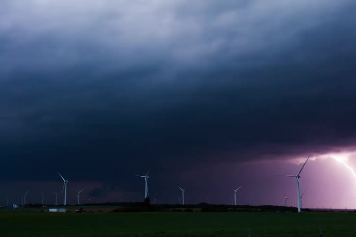 A lightning strike illuminating a dark and stormy sky over a field of wind turbines