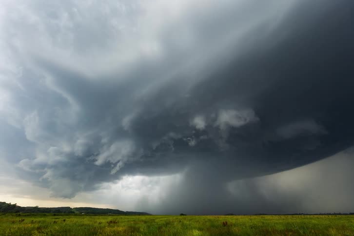 A tornado crawling across a grassland carrying debris beneath a dark cloudy sky