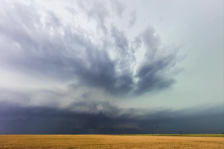 Lightning flashes as dark storm clouds move in rotation across the rural landscape with cars on the road