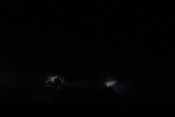 A dramatic timelapse video shows a dark stormy night sky with bursts of lightning the lightning flashes within the clouds and illuminates the landscape below