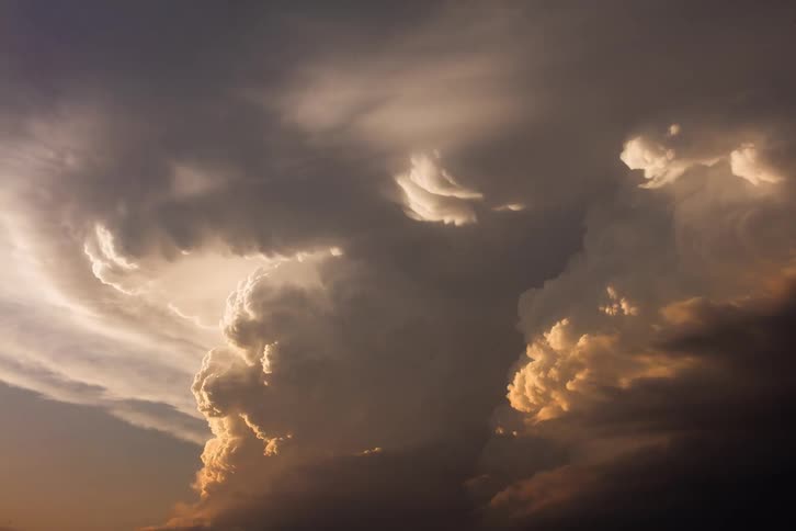 A powerful thunderstorm builds with towering cumulonimbus clouds their tops brightly lit by the setting sun while their undersides are dark and ominous against a dramatic sky