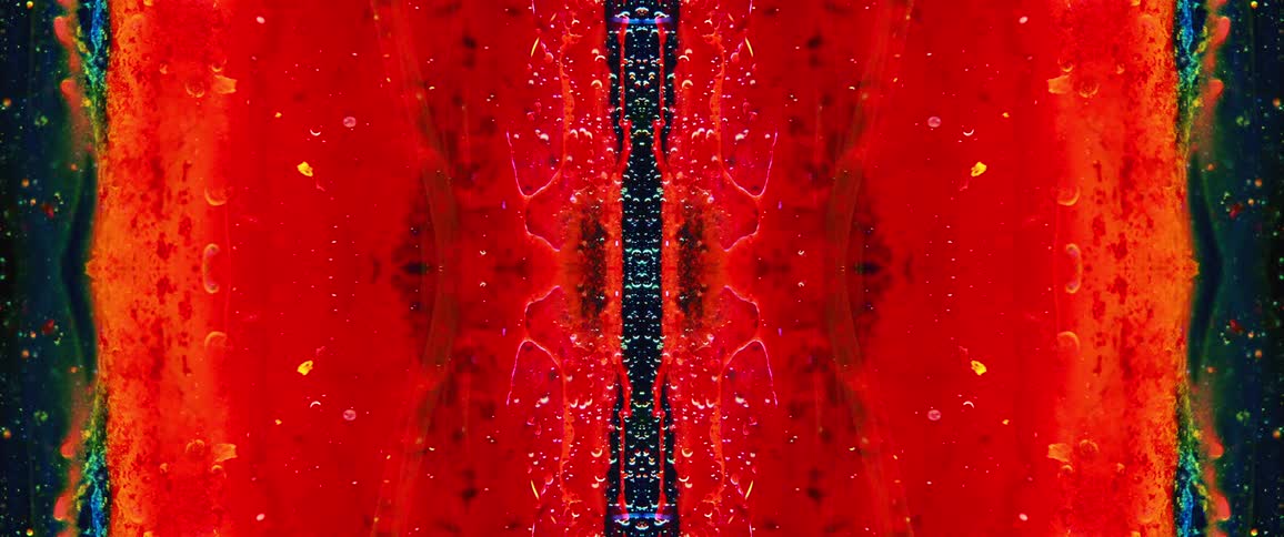 An abstract symmetrical pattern of pulsing and morphing red light with an internal blue and green glow creating a kaleidoscope effect on a black background