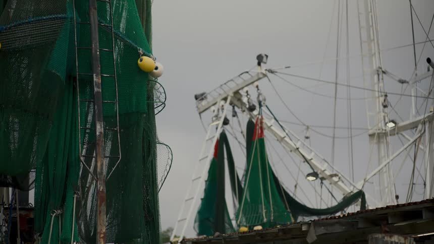 A view of the top portion of a fishing boat shows the rigging and nets with a bright green net and yellow buoys hanging on the left and a darker green and red net hanging in the center