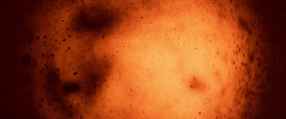 The video shows an abstract macro shot of a liquid likely a beer or an ambercolored fluid as it bubbles and settles the liquid is a vibrant orangeyellow color at the beginning of the video several large dark oddly shaped bubbles float on the sur