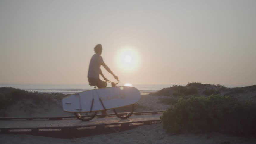 The man rides his bike carrying a surfboard on the beach