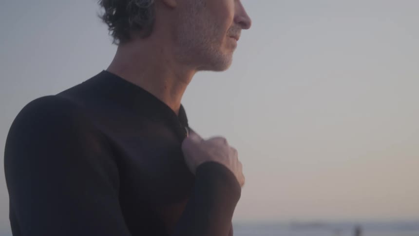 The man zips up his wet suit on the beach