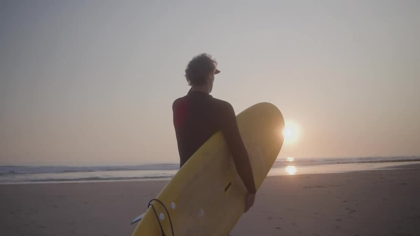 The man is holding his surfboard on the beach