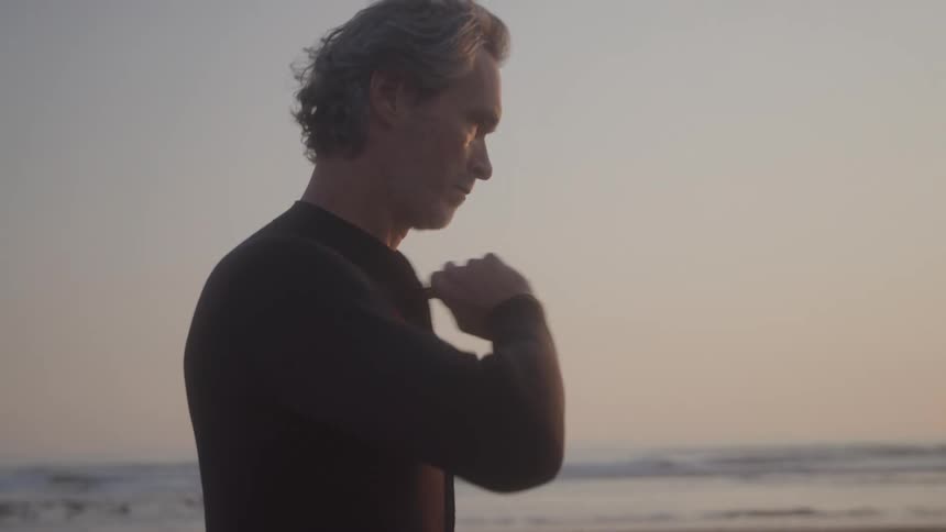 An in a wetsuit looking at the sea during sunset